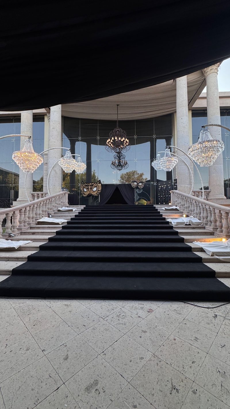 Entrada de evento con alfombra negra, columnas blancas y candelabros de cristal