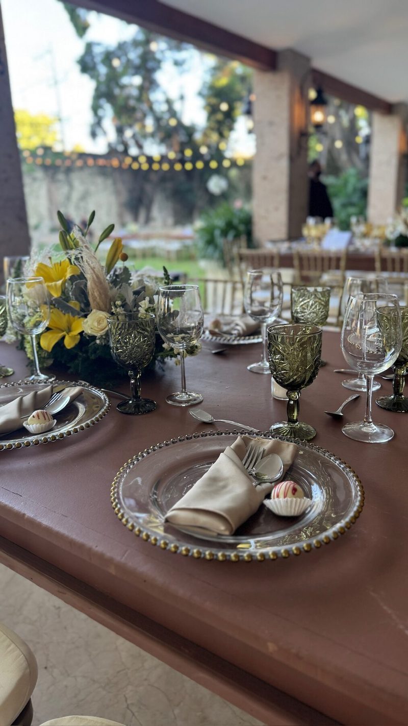 Mesa de boda en jardín con copas verdes y centro floral con velas