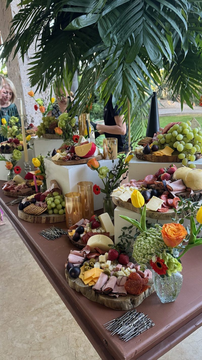 Mesa de grazing con quesos, fruta y flores blancas y amarillas