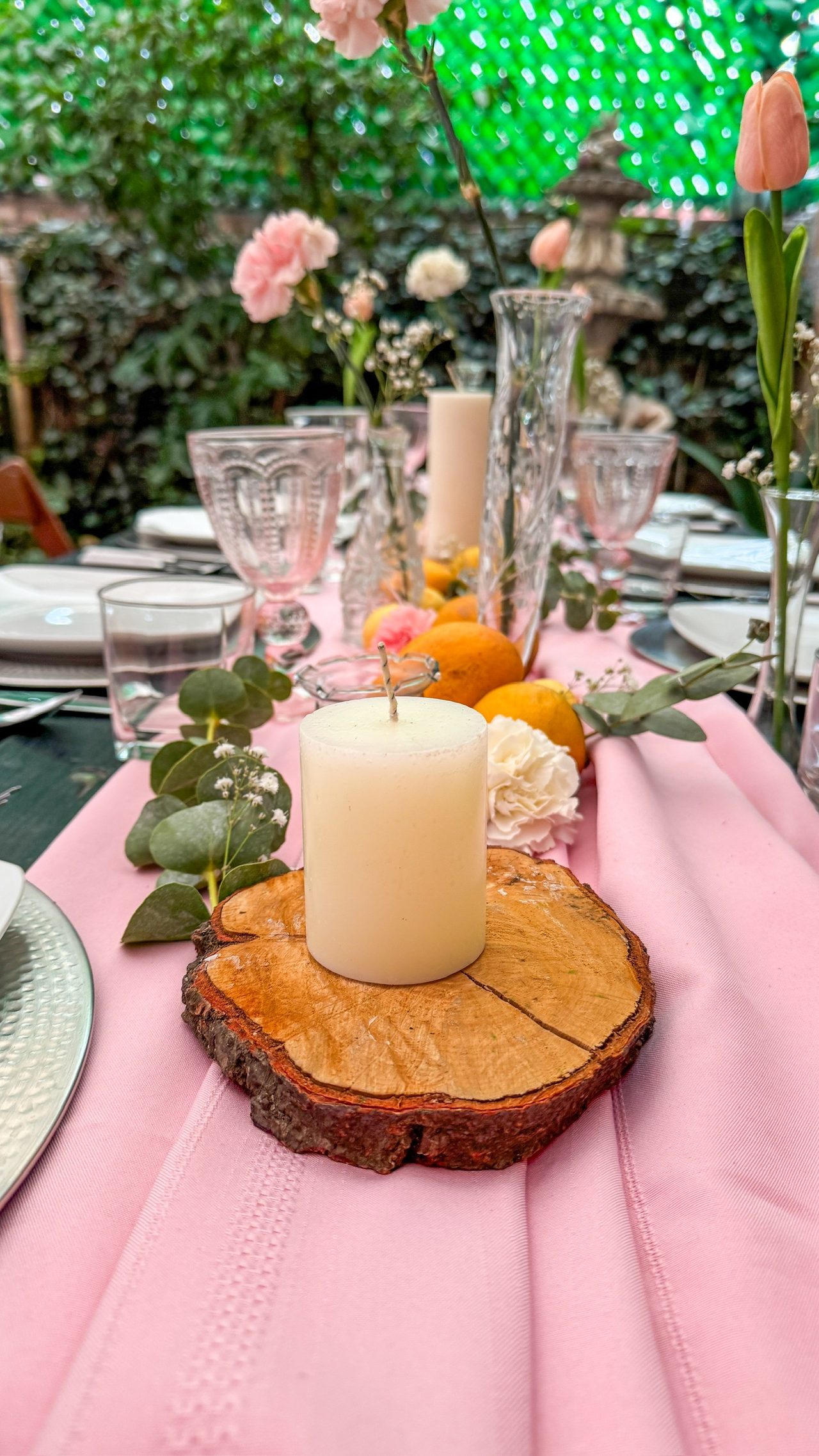 Mesa vestida en rosa con vela sobre rodaja de madera, tulipanes y cítricos