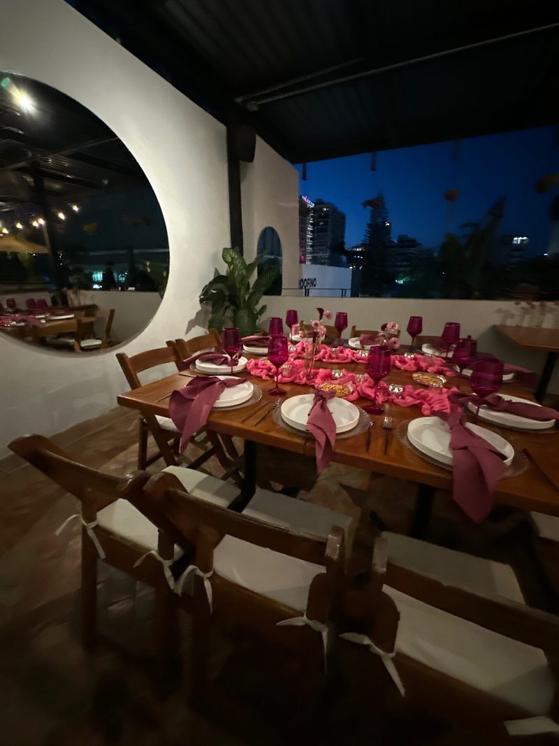 Terraza con mesa vestida en tonos vino, ventana circular y vista nocturna