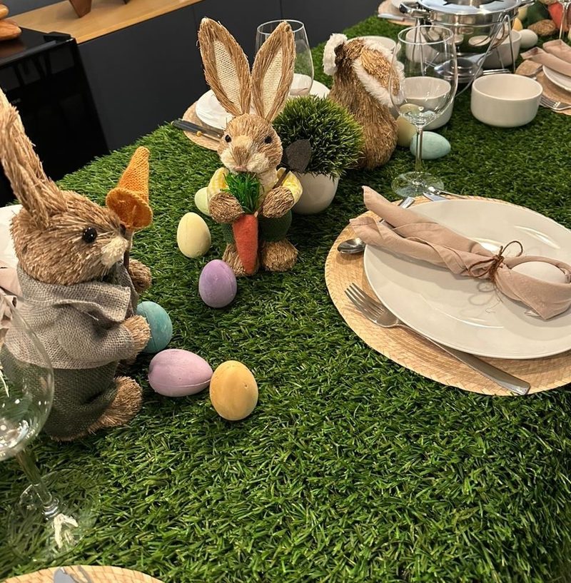Mesa temática de Pascua con camino de pasto, conejos decorativos y huevos en tonos pastel