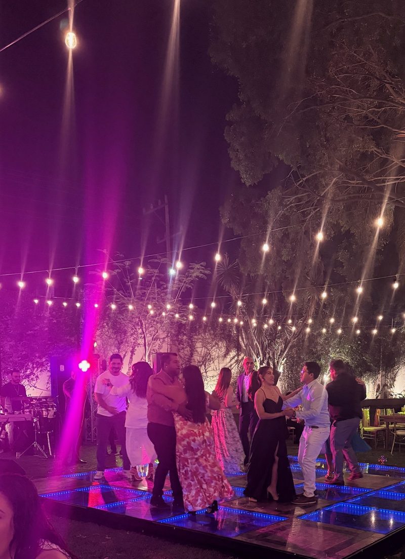 Invitados bailando en una pista iluminada en un jardín, bajo series de luces cálidas por la noche