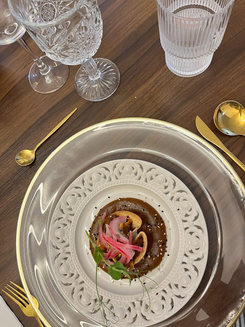Plato gourmet servido en vajilla decorada con cubiertos dorados, visto desde arriba