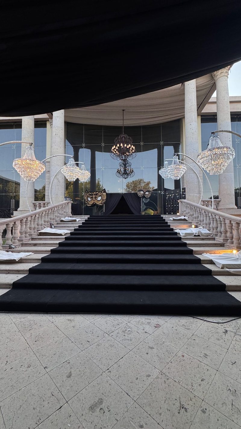 Entrada de XV años con escalinata alfombrada, columnas de piedra y máscaras venecianas doradas