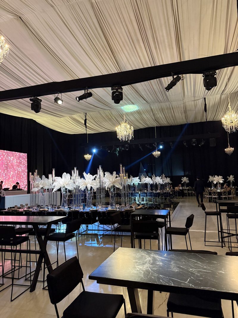 Salón de XV años con techo drapeado, centros de plumas blancas y pantalla iluminada en rosa